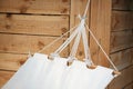 Close-up of a white hammock made of natural fabric on a wooden base hanging on ropes against a wooden wall, concept of natural