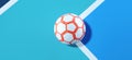 Close-up of a white orange futsal ball in the corner of a blue soccer field background