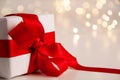 Close up of white paper gift box with a red satin ribbon bow on bright background with golden bokeh. Holidays greeting cards and Royalty Free Stock Photo