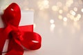 Close up of white paper gift box with a red satin ribbon bow on bright background with golden bokeh. Holidays greeting cards and Royalty Free Stock Photo