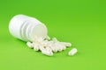 Close up white pill bottle with spilled out capsules on green background with copy space. Focus on foreground, soft bokeh. Pharmac