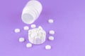 Close up white pill bottle with spilled out pills and capsules in cap on purple background with copy space. Focus on foreground, s Royalty Free Stock Photo