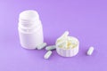 Close up white pill bottle with spilled out pills and capsules in cap on purple background with copy space. Focus on foreground, s Royalty Free Stock Photo