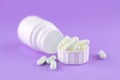 Close up white pill bottle with spilled out pills and capsules in cap on purple background with copy space. Focus on foreground, s Royalty Free Stock Photo