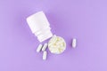 Close up white pill bottle with spilled out pills and capsules in cap on purple background with copy space. Focus on foreground, s Royalty Free Stock Photo