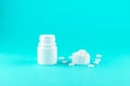 Close up white pill bottle with spilled out pills and capsules in cap on turquoise background with copy space. Focus on foreground Royalty Free Stock Photo