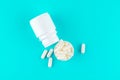 Close up white pill bottle with spilled out pills and capsules in cap on turquoise background with copy space. Focus on foreground Royalty Free Stock Photo