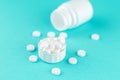 Close up white pill bottle with spilled out pills and capsules in cap on turquoise background with copy space. Focus on foreground Royalty Free Stock Photo