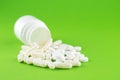 Close up white pill bottle with spilled out pills and capsules on green background with copy space. Focus on foreground, soft boke Royalty Free Stock Photo