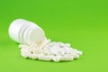 Close up white pill bottle with spilled out pills and capsules on green background with copy space. Focus on foreground, soft boke Royalty Free Stock Photo