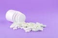 Close up white pill bottle with spilled out pills and capsules on purple background with copy space. Focus on foreground, soft bok Royalty Free Stock Photo