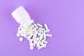 Close up white pill bottle with spilled out pills and capsules on purple background with copy space. Focus on foreground, soft bok Royalty Free Stock Photo