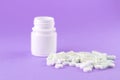 Close up white pill bottle with spilled out pills and capsules on purple background with copy space. Focus on foreground, soft bok Royalty Free Stock Photo