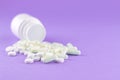 Close up white pill bottle with spilled out pills and capsules on purple background with copy space. Focus on foreground, soft bok Royalty Free Stock Photo