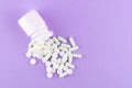 Close up white pill bottle with spilled out pills and capsules on purple background with copy space. Focus on foreground, soft bok Royalty Free Stock Photo