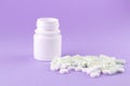 Close up white pill bottle with spilled out pills and capsules on purple background with copy space. Focus on foreground, soft bok Royalty Free Stock Photo