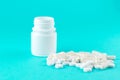 Close up white pill bottle with spilled out pills and capsules on turquoise background with copy space. Focus on foreground, soft Royalty Free Stock Photo