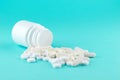 Close up white pill bottle with spilled out pills and capsules on turquoise background with copy space. Focus on foreground, soft Royalty Free Stock Photo