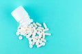 Close up white pill bottle with spilled out pills and capsules on turquoise background with copy space. Focus on foreground, soft Royalty Free Stock Photo