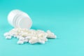 Close up white pill bottle with spilled out pills and capsules on turquoise background with copy space. Focus on foreground, soft Royalty Free Stock Photo