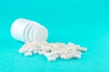 Close up white pill bottle with spilled out pills and capsules on turquoise background with copy space. Focus on foreground, soft Royalty Free Stock Photo