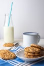 Close-up of white plate with chocolate chip cookies, cup, spoon and bottle of milk with blue straw, on blue napkin and white backg Royalty Free Stock Photo