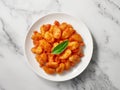 Close-up of a white plate of cooked POTATO GNOCCHI in tomato sauce and with basil. Light marble background. Top view. One object Royalty Free Stock Photo