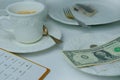 Close-up of white plate for money, American dollars banknotes and coins, Restaurant bill, cup of coffee, delicate pink flowers,