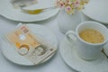 Close-up of a white plate for money, British pounds banknotes and coins, Restaurant bill, cup of coffee, delicate pink flowers,