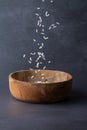 Close-up of white rice falling into wooden bowl on gray background, vertical