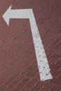 Close-up of white road marking arrow pointing to left on maroon paving flag Royalty Free Stock Photo