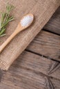 Close-up of white rock salt in wooden spoon by rosemary on jute fabric at table