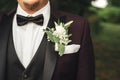 Close up of white rose wedding boutonniere on groom`s lapel of black suit. Outdoor photo, blurred green foliage Royalty Free Stock Photo