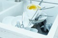 Close-up of white sink full of dirty white tableware, ceramic plates, bowls, knives, forks, spoons, grey cups. Cleaning. Royalty Free Stock Photo