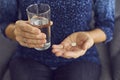 Close up of white soluble aspirin pill and glass of water in hands of unknown woman.