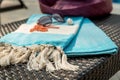 Close-up of white and turquoise Turkish towel, sunglasses, orange necklace and straw hat on rattan lounger.