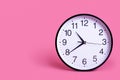 Close-up White wall clock on a light pastel pink background. The concept \