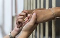 Woman holding the hand of a male prisoner in a white cage