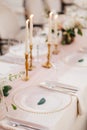 Wedding dinner table reception. Close-up of wildcard with gold beads, transparent glass. Runner of pink silk. Candles in Royalty Free Stock Photo