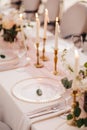 Wedding dinner table reception. Close-up of wildcard with gold beads, transparent glass. Runner of pink silk. Candles in