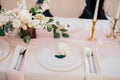 Wedding dinner table reception. Close-up of wildcard with gold beads, transparent glass. Runner of pink silk. Candles in