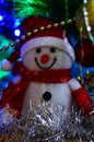 Close-up of a winter white toy snowman with Christmas tinsel in the background