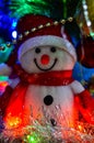 Close-up of a winter white toy snowman with Christmas tinsel in the background