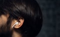 Close-up of wireless earphone in human ear on dark background. Royalty Free Stock Photo