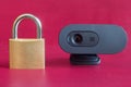 Close-up of a wireless webcam next to a closed old-fashioned gold padlock on a colorful red background.