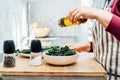 Close up woman adding olive oil while cooking kale chips or healthy salad for dinner on the kitchen table. Healthy Royalty Free Stock Photo