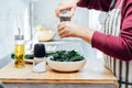 Close up woman adding spices and herbs while cooking kale chips or healthy salad for dinner on the kitchen table Royalty Free Stock Photo