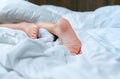 Close up woman bare feet on the bed over white blanket and bed sheet in the bedroom of home or hotel. Sleeping and relax concept. Royalty Free Stock Photo