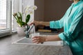Close-up of a woman collects water in a plastic glass from the tap in the kitchen sink in front of the window