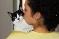 Woman with curly hair holding and kissing her domestic black and white kitten with green eyes on the shoulder. Concept